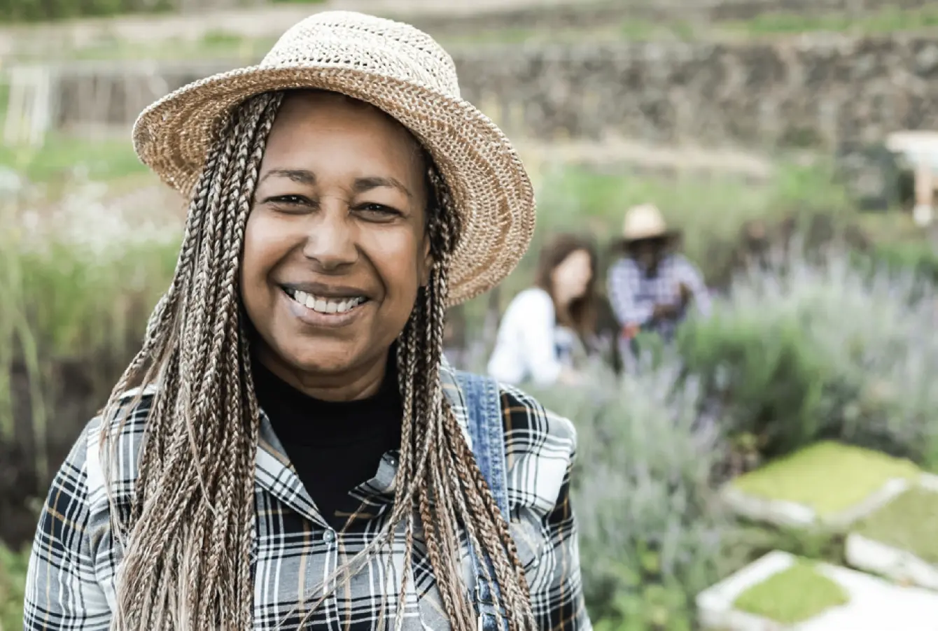 A smiling gardener in the foreground with two other gardeners crouched next to the crop, out of focus in the background.